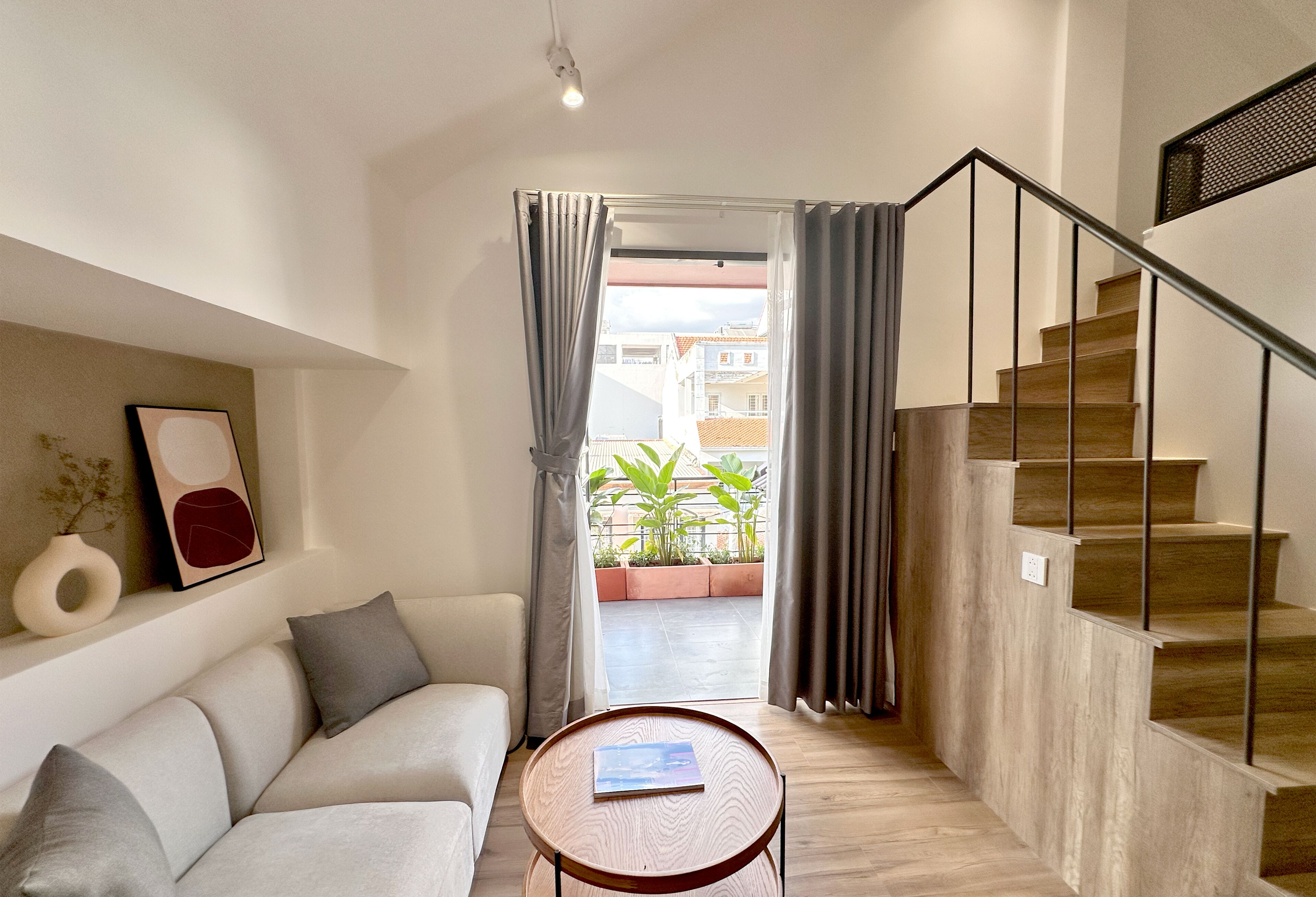 A modern living room with a sofa, a small round table, and a staircase leading to an outdoor area with plants.