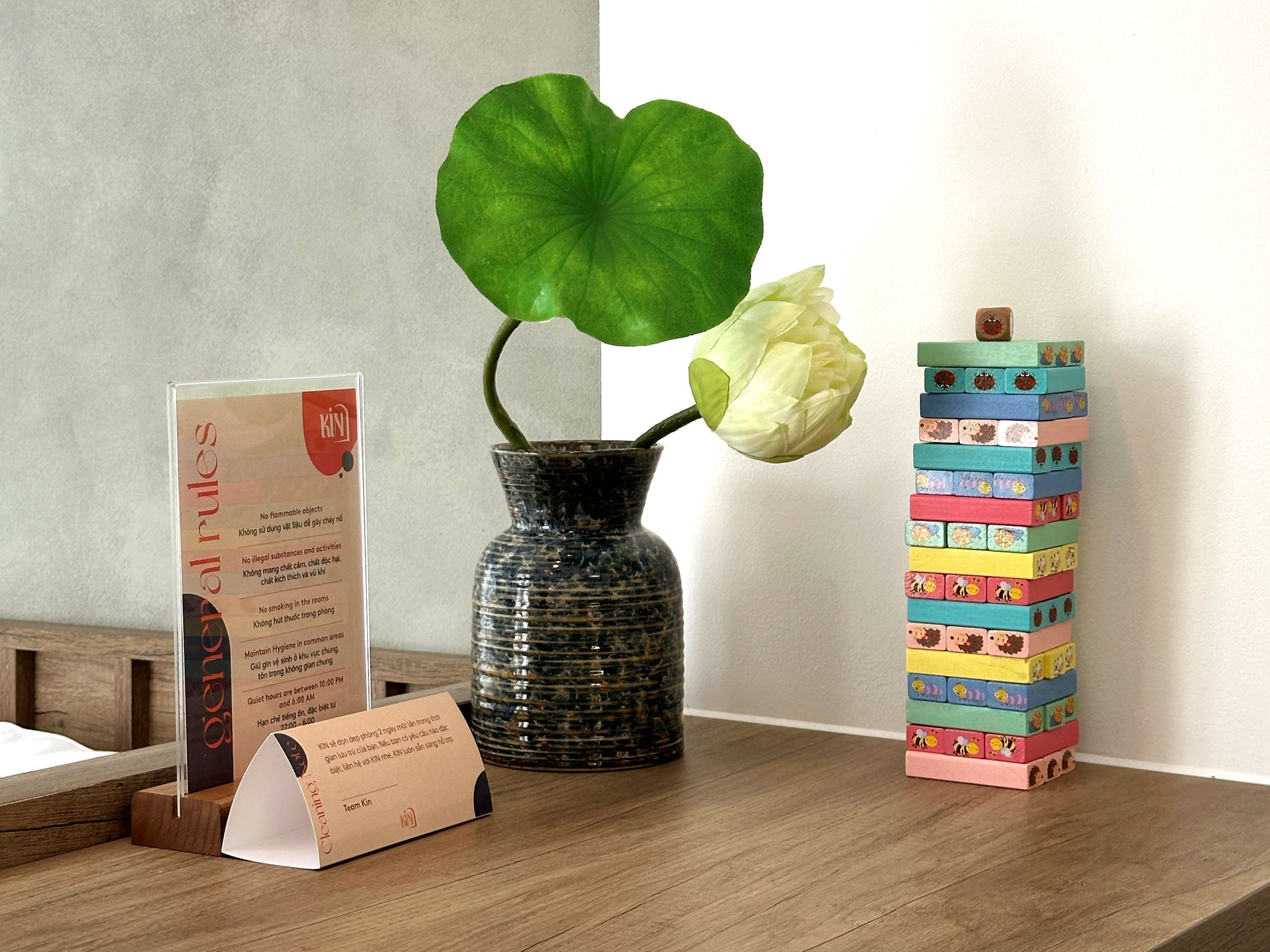 A wooden table with a vase containing a single white flower, a stack of colorful wooden blocks, and a sign with text.