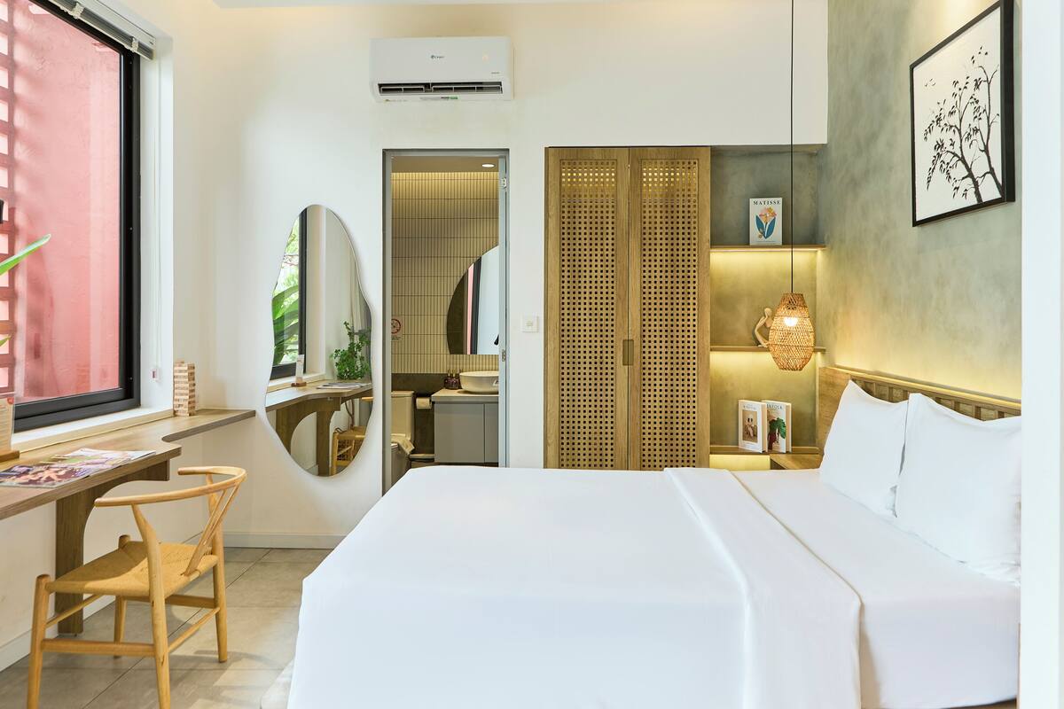 Une chambre d’hôtel comprenant un lit, un bureau, une chaise, un miroir, une armoire, une lampe suspendue et un climatiseur fixé au mur.