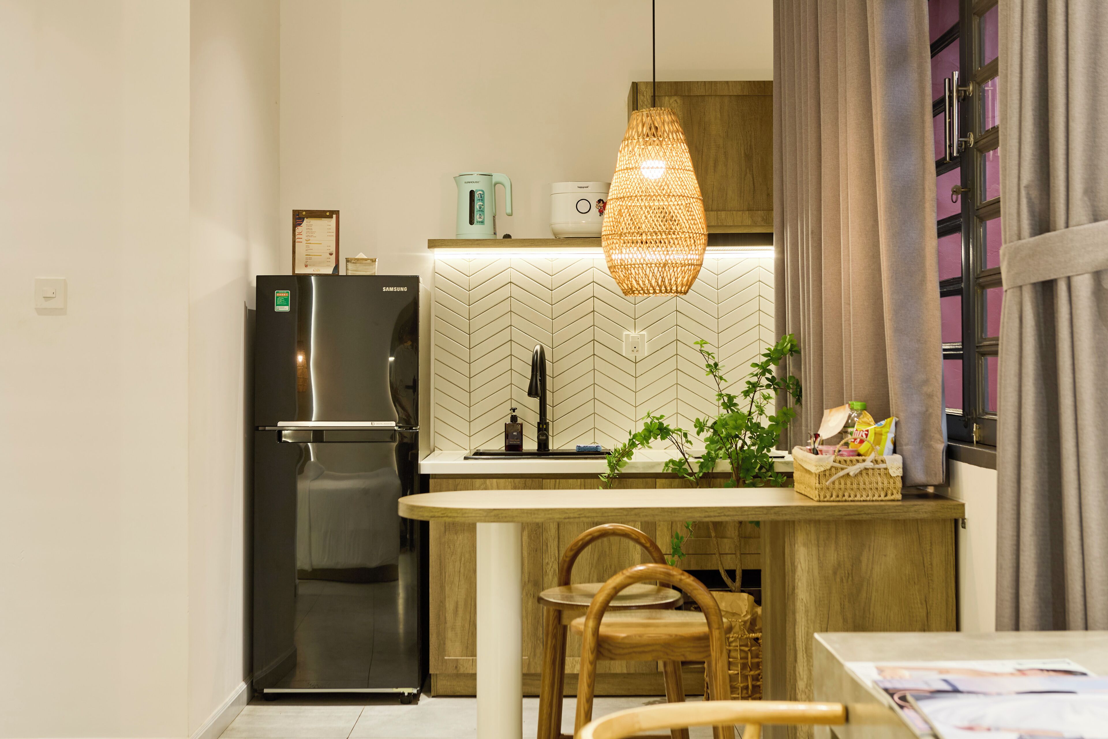 A modern kitchen with a refrigerator, a coffee maker, and a hanging light fixture.