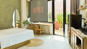 Une chambre d’hôtel moderne équipée d’un lit, d’un bureau, d’un écran de télévision affichant « NETFLIX » et offrant une vue sur l’extérieur.