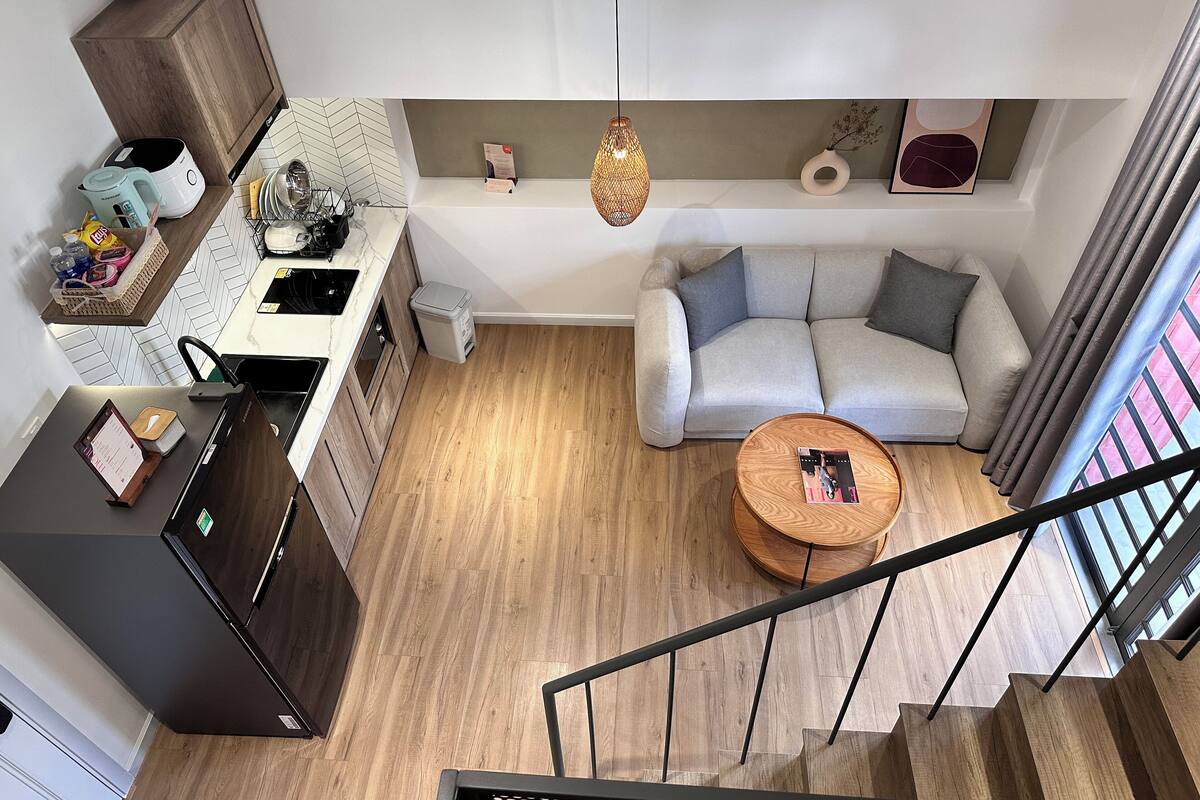 Une cuisine moderne dotée d’un four encastré, un coin repas avec une table en bois, un canapé gris et un escalier menant à l’étage supérieur.