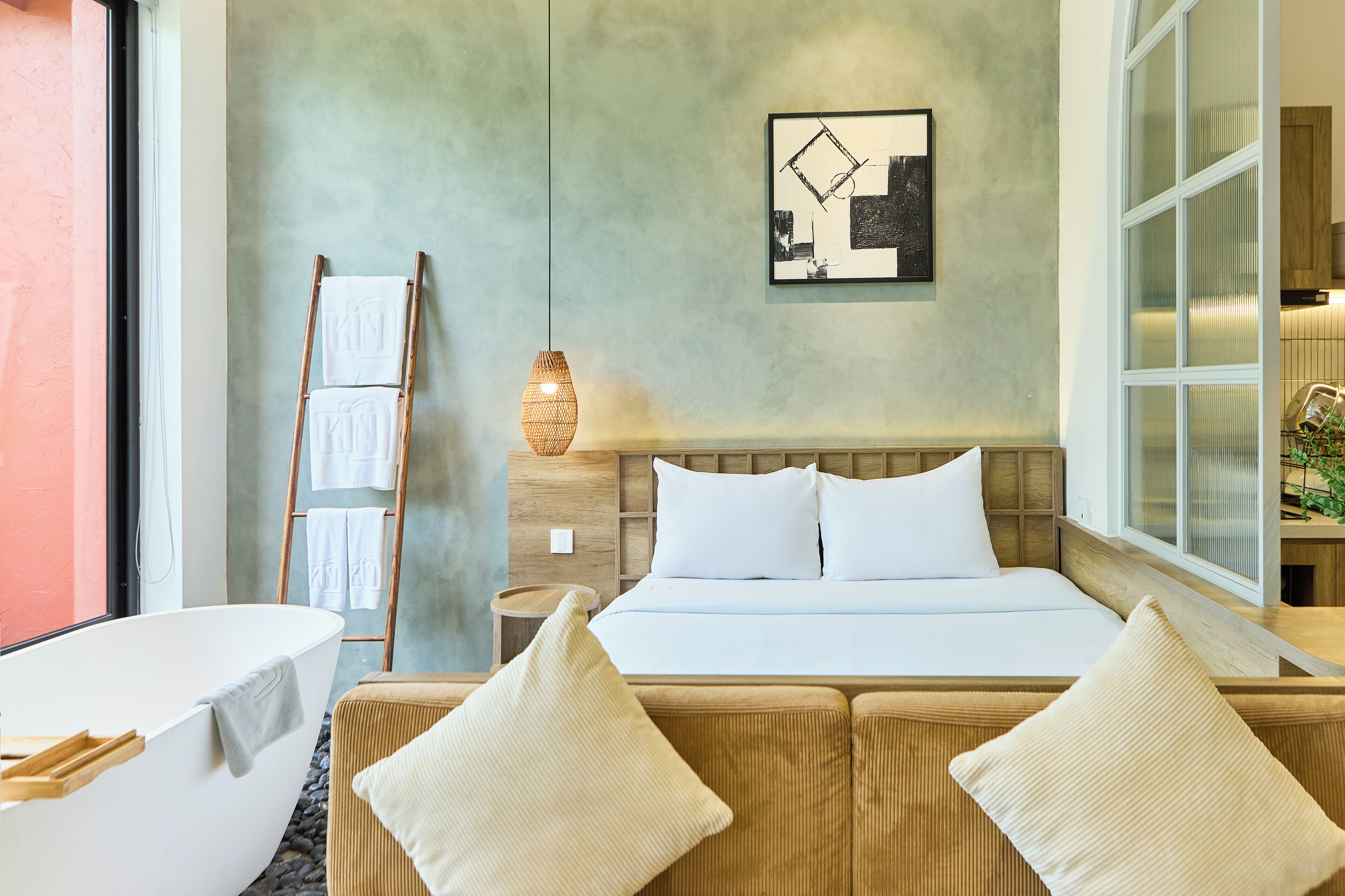 Habitación de hotel moderna con una cama grande, cabecera de madera, mesita de noche con lámpara y vistas al exterior.