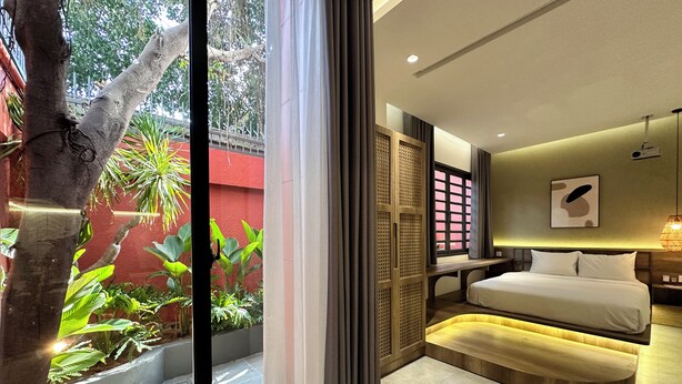 Une chambre d’hôtel moderne, équipée d’un lit, d’une table de chevet et offrant une vue sur la verdure environnante.