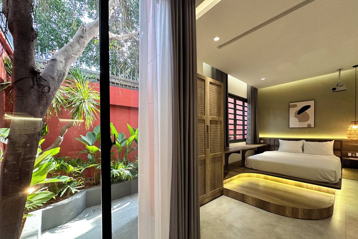 Une chambre d’hôtel moderne, équipée d’un lit, d’une table de chevet et offrant une vue sur la verdure environnante.