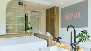 Une chambre d’hôtel moderne avec un grand lit, une baignoire, une armoire en bois et un panneau Netflix fixé au mur.