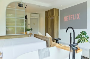 Habitación de hotel moderna con una cama grande, una bañera, un armario de madera y un letrero de Netflix montado en la pared.