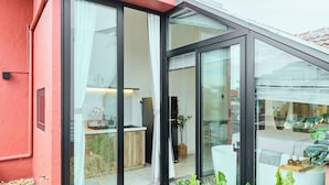 Une maison moderne dotée de grandes portes vitrées donnant sur une cuisine et un espace de vie, le tout entouré de galets et de plantes.