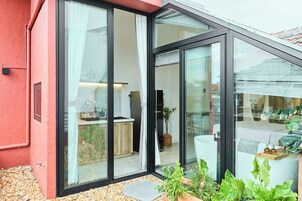 Una casa moderna con grandes puertas de vidrio que dan a una cocina y sala de estar, rodeada de piedras y plantas.