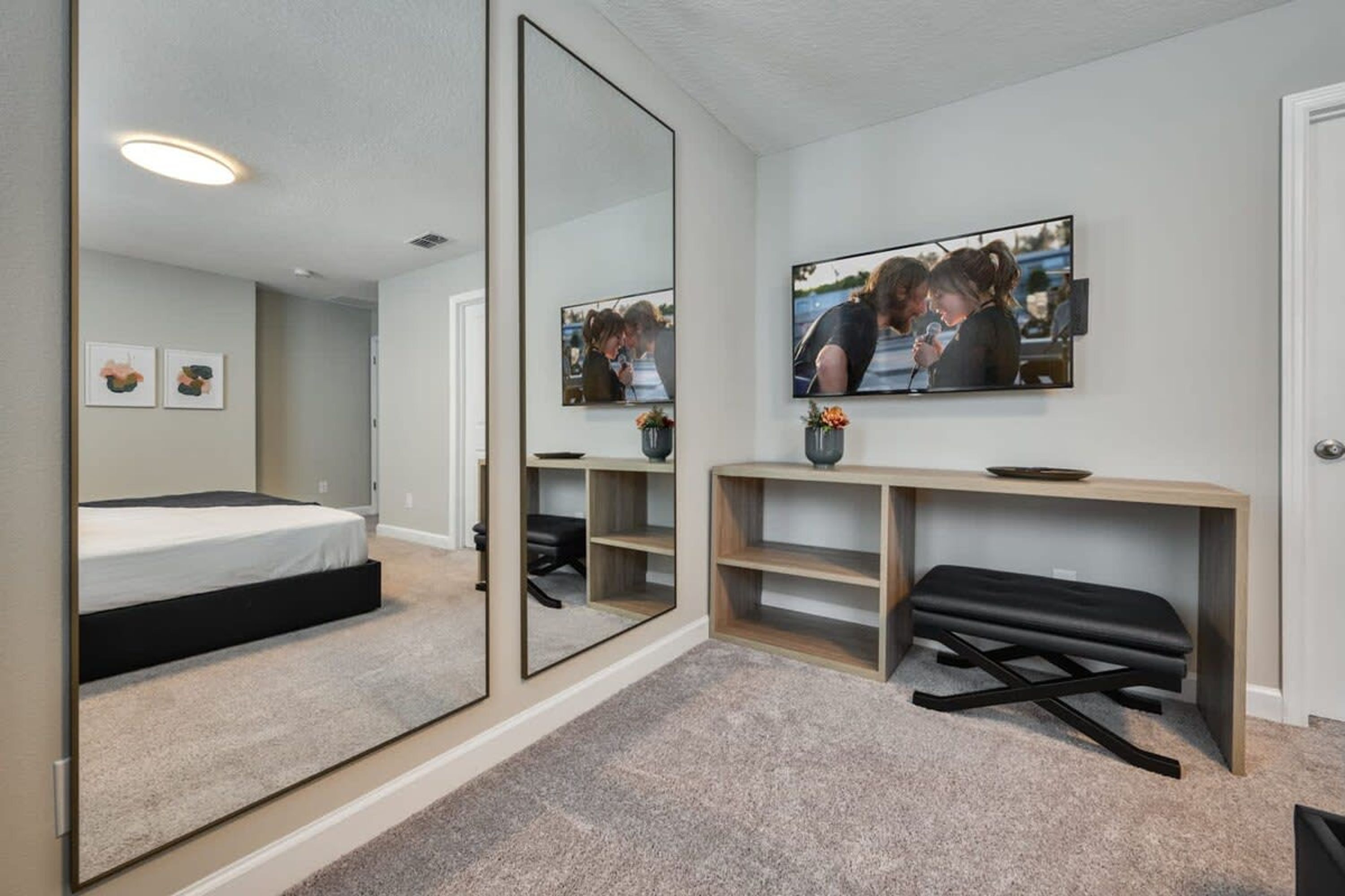 A modern bedroom with a bed, a large mirror, a TV, and a desk with a bench.