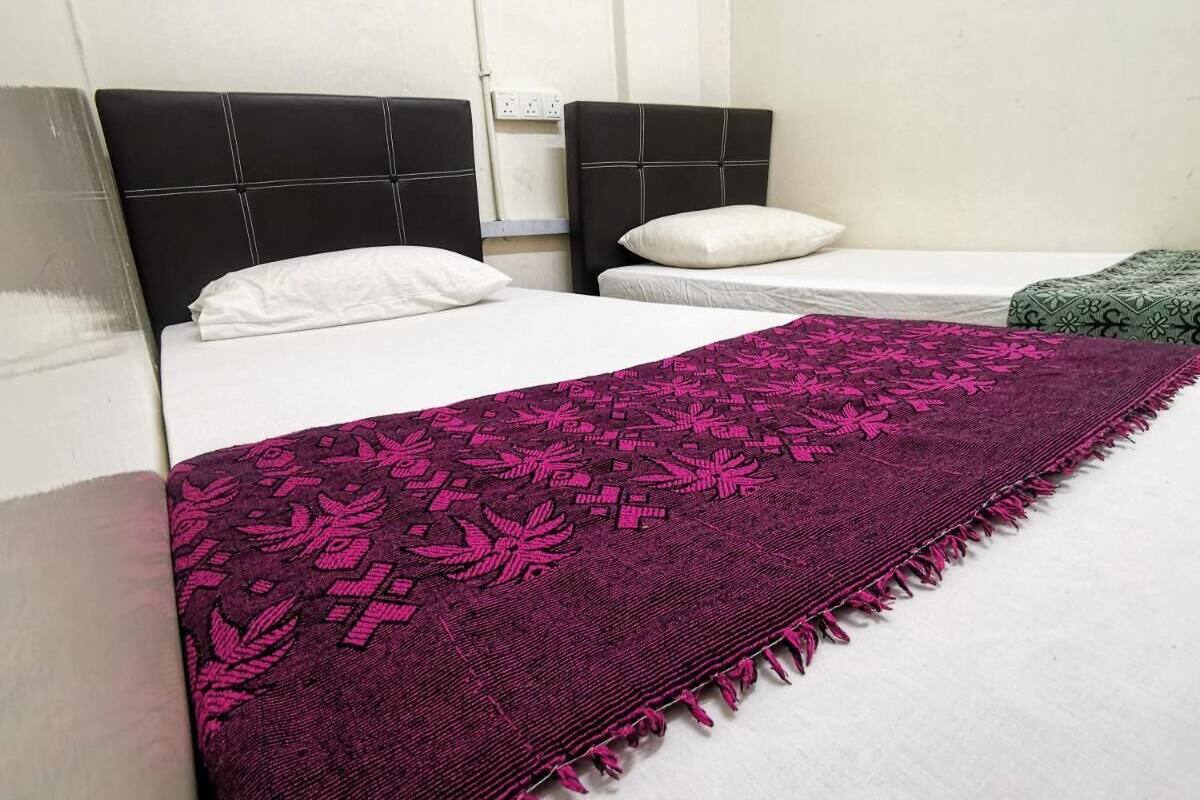 A hotel room with a bed, a black headboard, a white pillow, and a purple blanket with a leaf pattern.