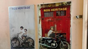 A hallway with two doors labeled 'ROS HERITAGE'. One door has a poster of a child on a bicycle, and the other door has a poster of a motorcycle. - OYO 90838 Ros Heritage Motel (George Town)