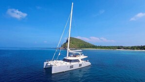 A white yacht on calm blue waters with a clear sky and a green island in the background. - El Nido (El Nido)