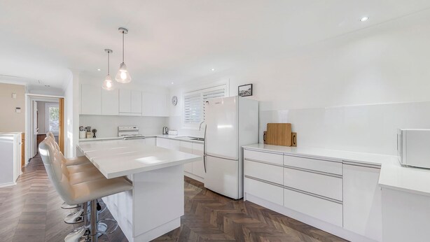 Une cuisine moderne avec des meubles blancs, un îlot central et des luminaires suspendus.