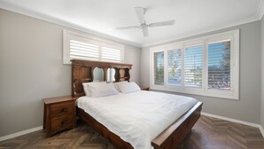 Une chambre à coucher avec un lit en bois, une table de chevet, un ventilateur de plafond et une fenêtre avec des stores.