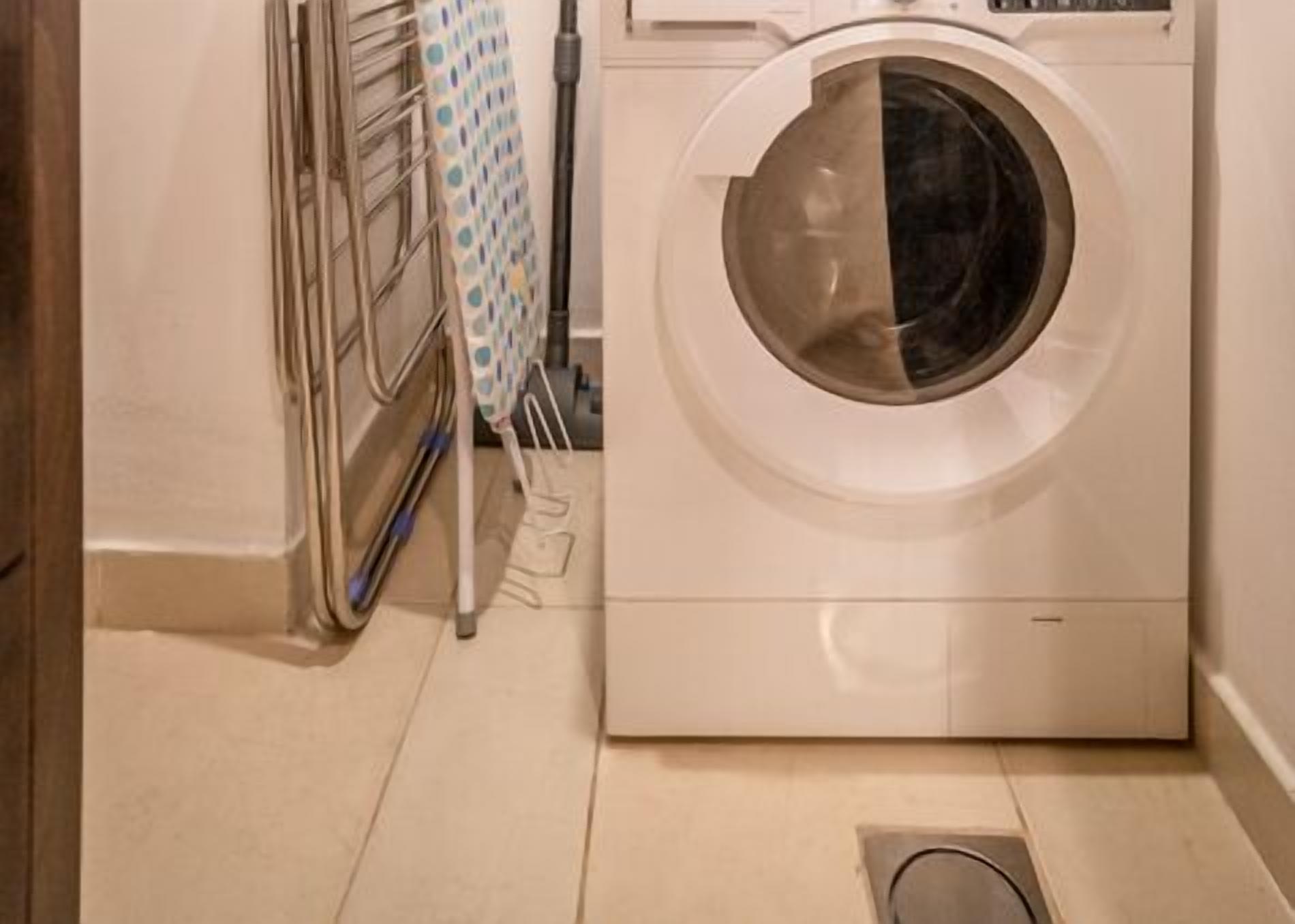 A compact laundry room with a front-loading washing machine, a drying rack, and a metal shelf unit.