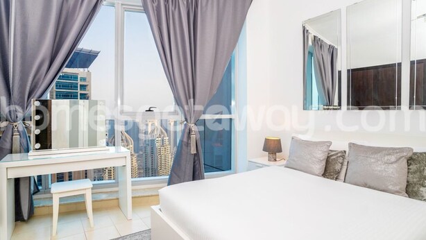 A modern hotel room with a large bed, a desk, and a view of the cityscape through the window. - HomesGetaway-Torch Marina Dubai Cozy 2BR (Dubai)