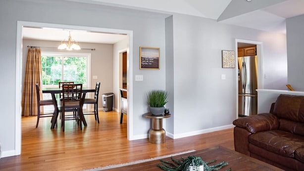 A spacious living room with a brown leather sofa, a dining area with a wooden table and chairs, and a kitchen with stainless steel appliances.