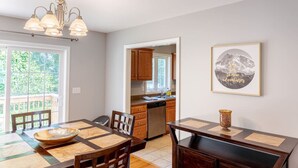 A dining area with a table, chairs, and a chandelier. There is a kitchen visible through an open doorway.