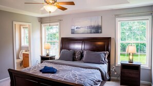 A bedroom with a bed, a ceiling fan, two bedside tables with lamps, a window, and a door.