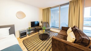 A modern hotel room with a bed, a sofa, a TV, a small table, and a large window with curtains.