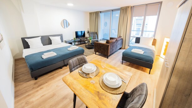 A hotel room with a bed, a sofa, a dining table with plates and glasses, a TV, and a window with curtains.