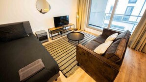 A modern hotel room with a sofa, a bed, a TV, and a balcony with a view of buildings.