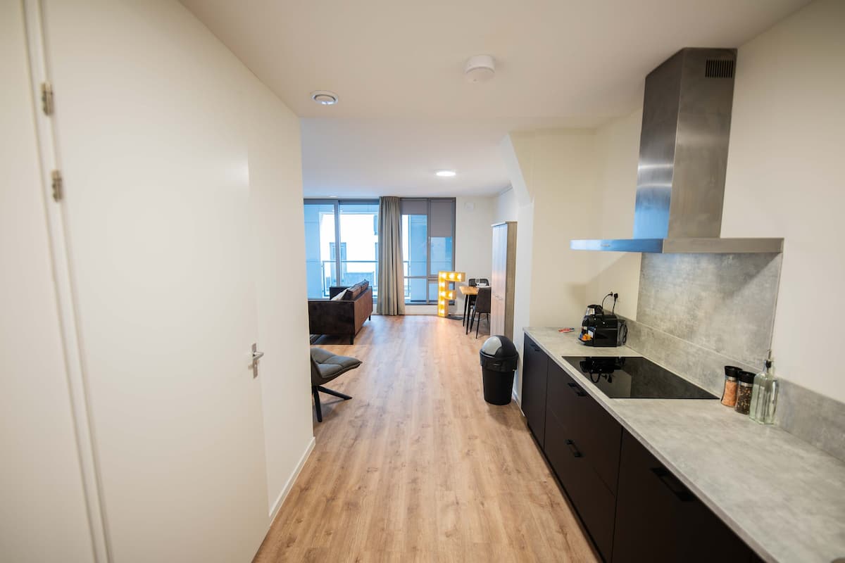 A modern kitchen with a wooden floor, a stainless steel range hood, and a countertop with jars.