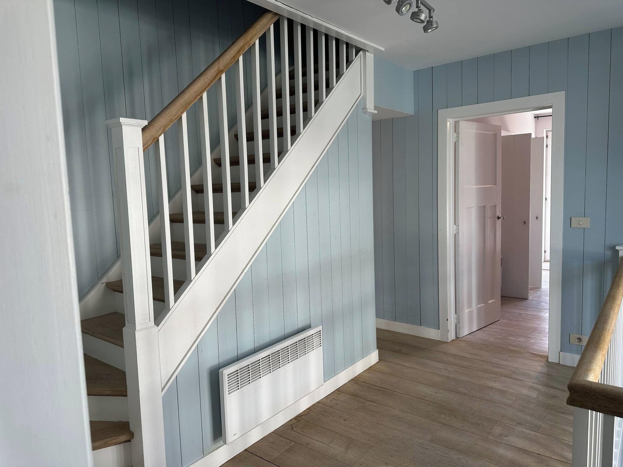 A staircase with white railings and a wooden handrail, leading to a room with light blue walls and wooden flooring.