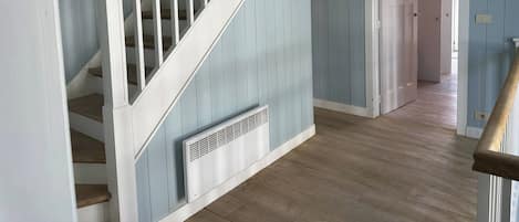 A staircase with white railings and a wooden handrail, leading to a room with light blue walls and wooden flooring.