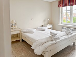 A neatly arranged bedroom with a bed, two bedside tables, a lamp, and a window with a view of buildings. - Luxurious 5-bedroom Holiday House in Knokke-heist Belgique (Knokke-Heist)