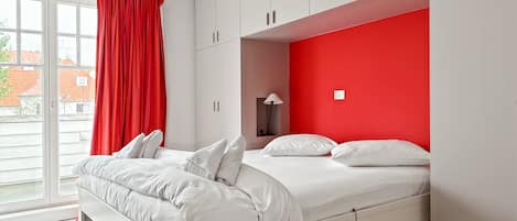Un dormitorio moderno con cama, paredes blancas y una pared decorada en rojo.