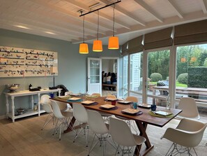 Un espace repas moderne avec une table en bois, des chaises blanches et une vue sur l’extérieur.