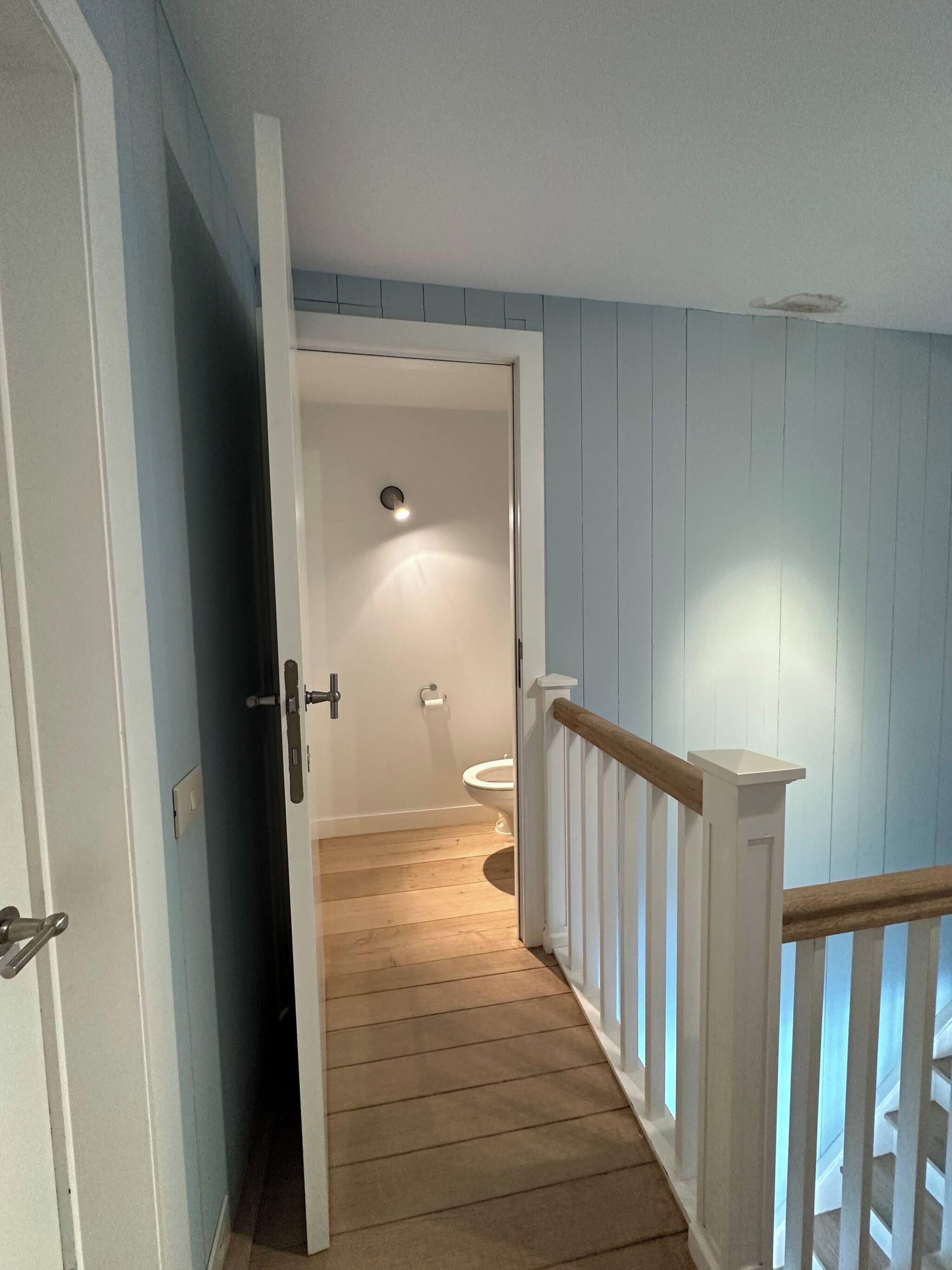 Ein Flur, der zu einem Badezimmer mit Toilette und einer Lampe führt.