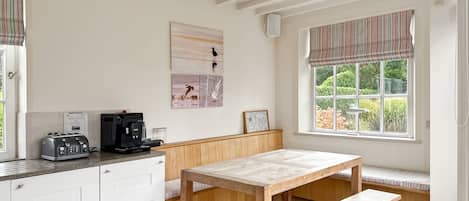 Una cocina con un banco de madera, una mesa y un ventanal con vistas a la vegetación.