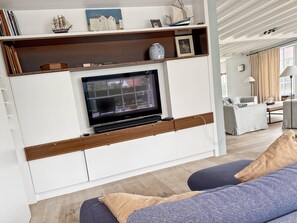 A modern living room with a flat-screen TV, wooden shelves, and a sofa.