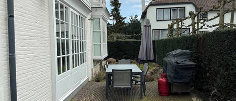 A residential backyard with a patio, a table and chairs, a covered grill, and a hedge.
