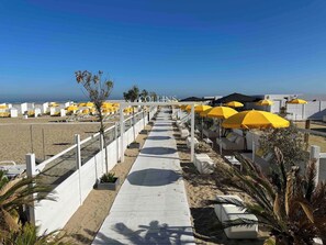 Un hôtel situé en bord de mer, avec une promenade bordée de parasols jaunes et de chaises longues blanches.