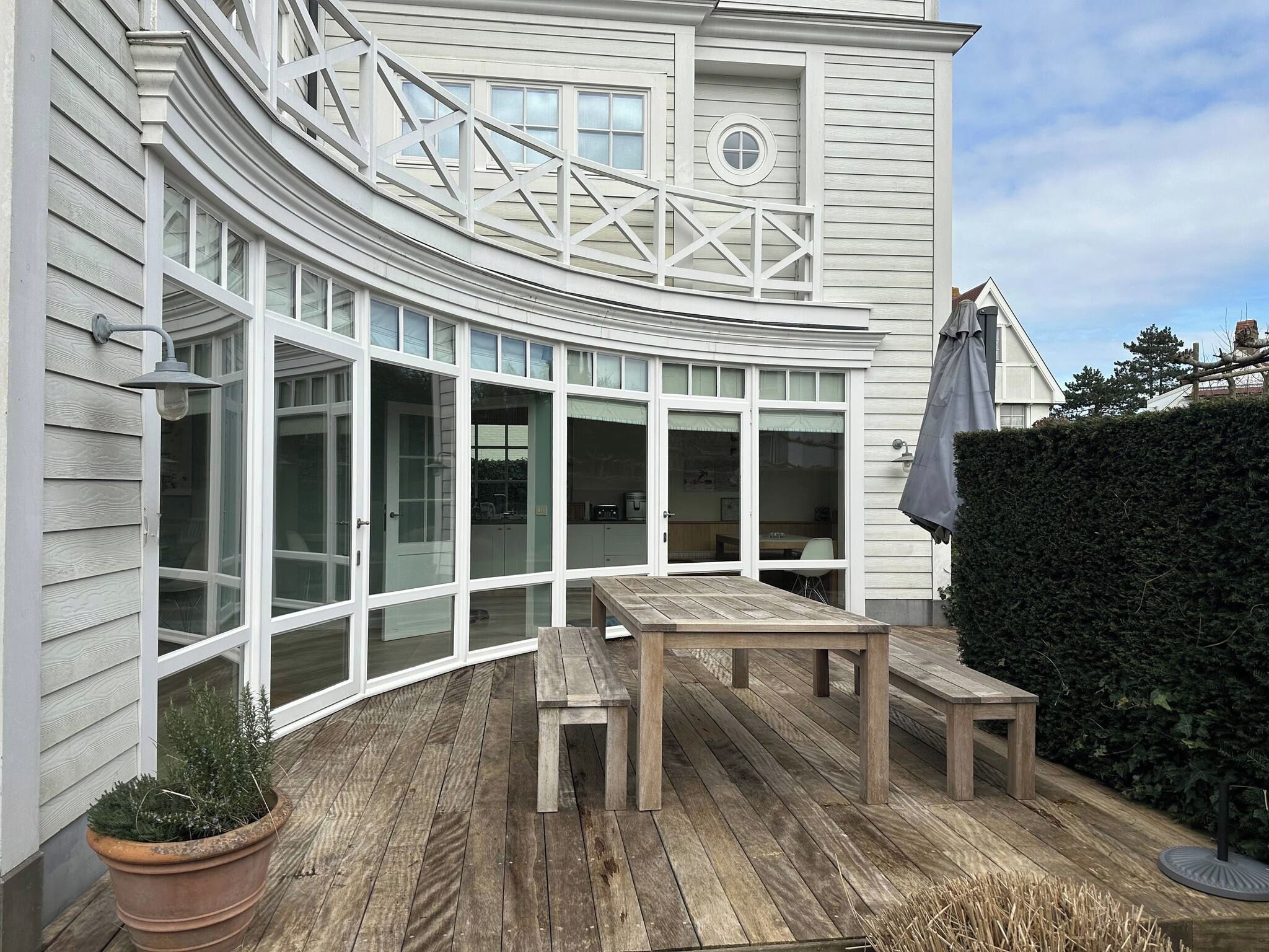 A curved exterior with large windows, a wooden deck, and a potted plant.