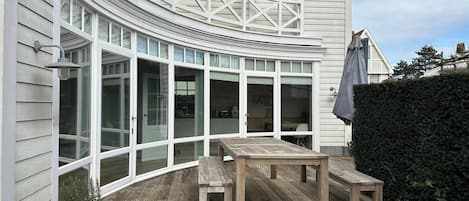 A curved exterior with large windows, a wooden deck, and a potted plant.