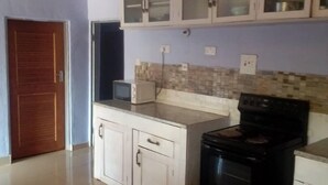 A kitchen with white cabinets, a black stove, and a tiled backsplash. - Zambia (Chipata)