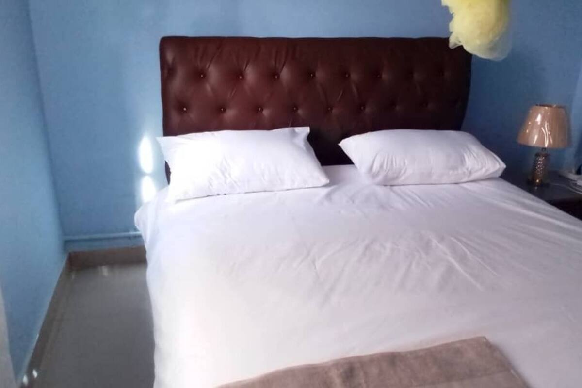 A neatly made bed with white linens and a brown headboard in a room with blue walls.