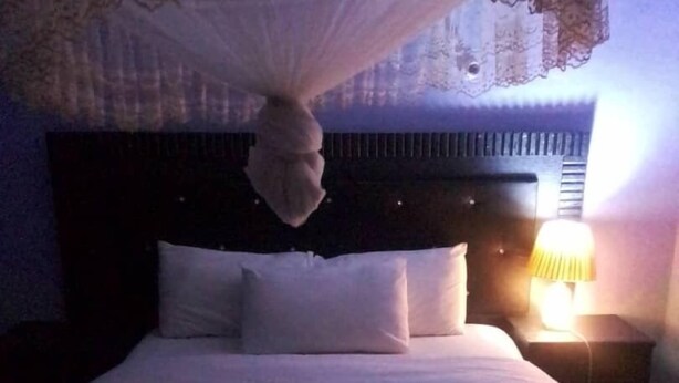 A bed with white linens, a dark headboard, and a bedside lamp. - Zambia (Chipata)