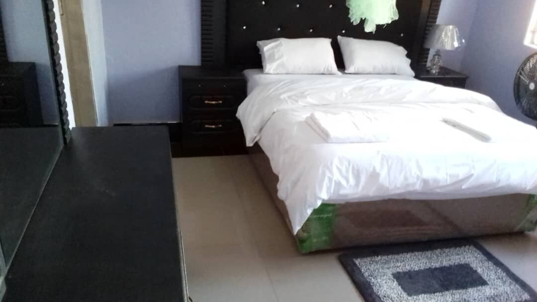 Una cama bien hecha con sábanas blancas, cabecera oscura y una mesita de noche con lámpara.