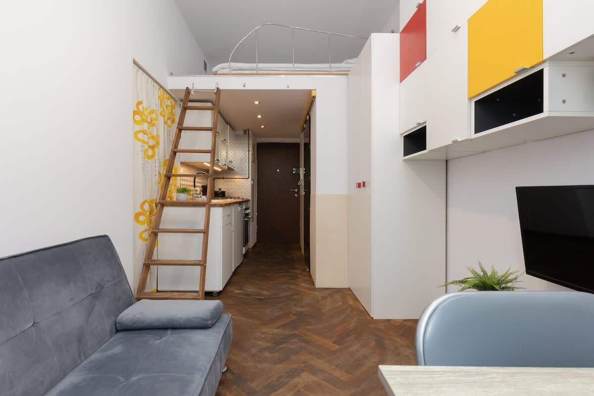 A compact living space with a sofa, a TV, a ladder leading to a loft, and a kitchenette.