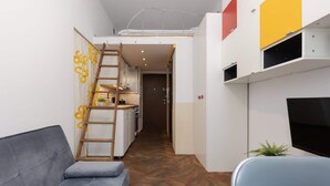 Un espacio habitable compacto con sofá, televisión, una escalera que lleva a un altillo y una kitchenette.
