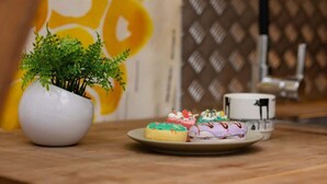 Una mesa de madera con un jarrón blanco que contiene una planta verde y un plato con pasteles de colores.