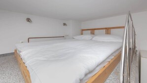 Una cama individual con estructura de madera y cabecera de metal, ropa de cama blanca y una mesita de noche pequeña.