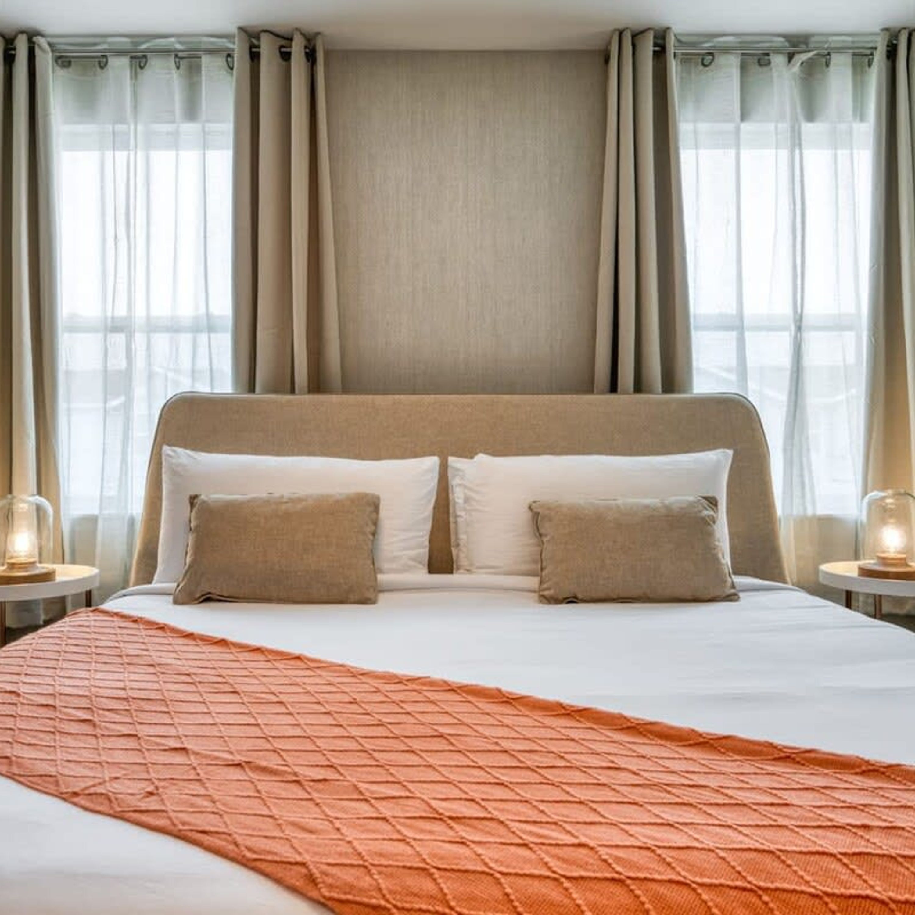 Ein Hotelzimmer mit einem großen Bett, zwei Nachttischen mit Lampen und transparenten Vorhängen.