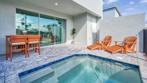 Una piscina con sillas y una mesa de madera, rodeada por un patio empedrado.